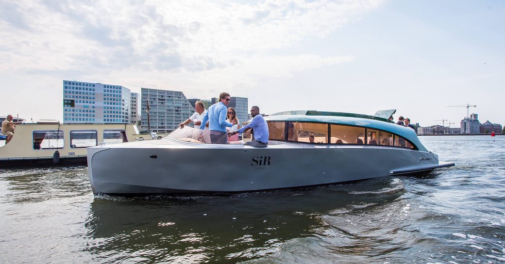 Limousine tender on still water with cityscape in background and people visible on board