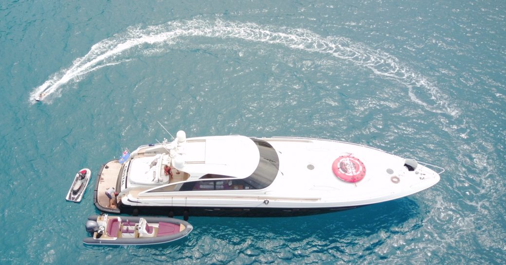 Large yacht, viewed from above with two tender boats adjacent to it and person waterskiing close by