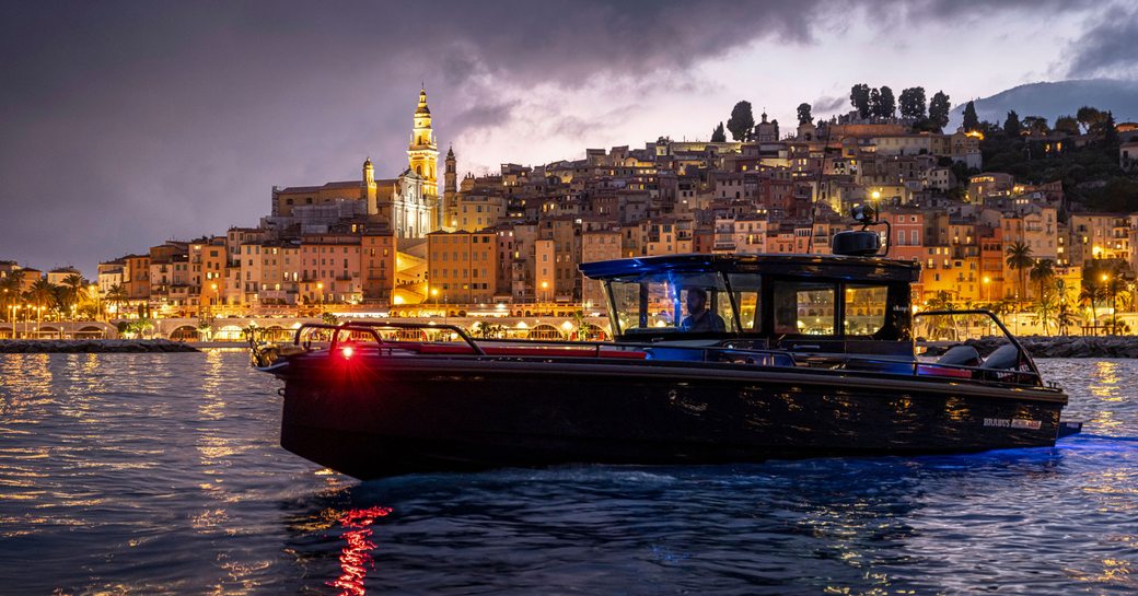 Chase boat on water at night with a city rising behind on a hill and buildings lit up