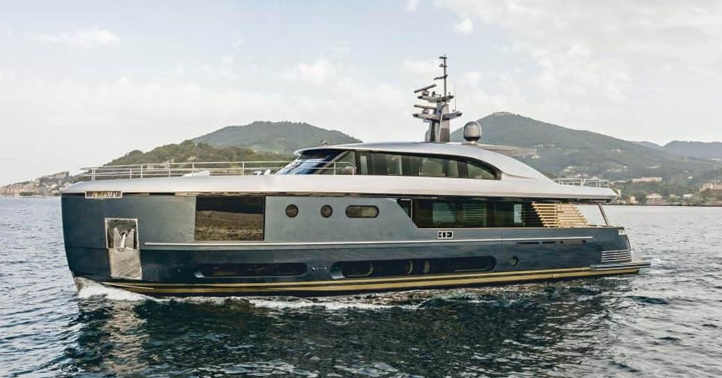 Azimut Magellano 30M semi displacement motor yacht running shot in calm waters with land in background, shot at water level along port side profile