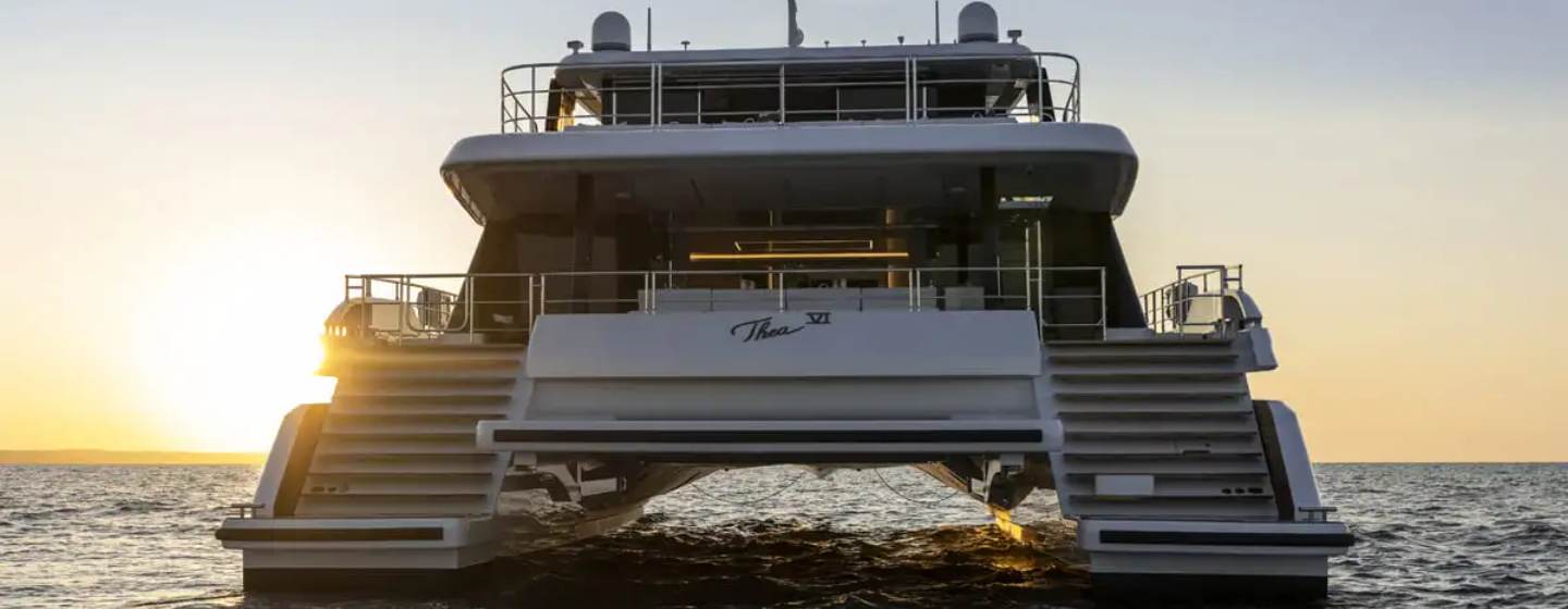 Sunreef Yacht THEA IV shown from water level towards the stern of the catamaran, it's approaching sunset as the sun is just low on the horizon in the backgroun