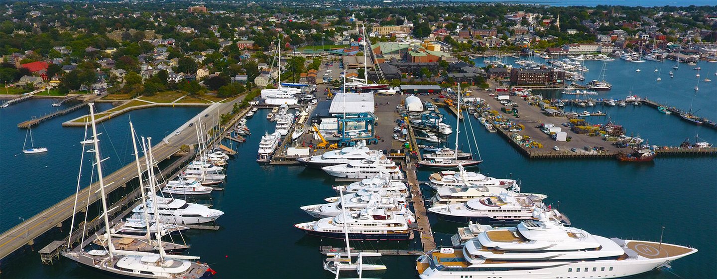Overview of Safe Harbor Newport Shipyard, multiple motoryachts berthed, surrounded by sea and City of Newport in background