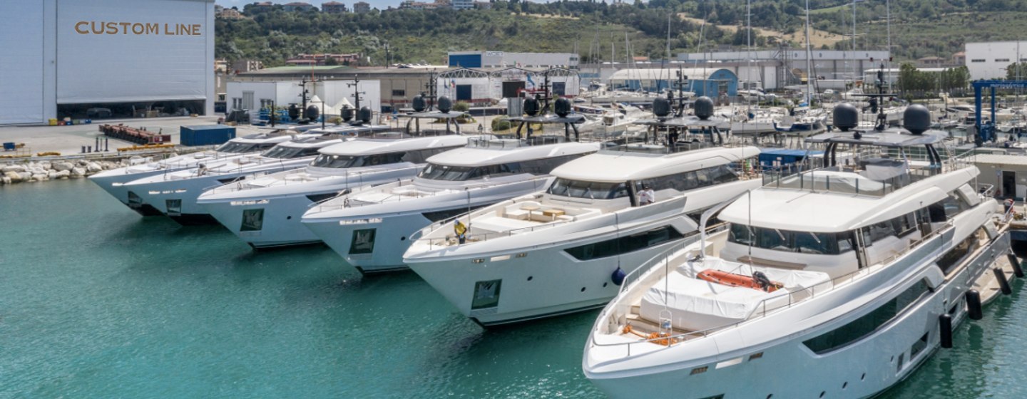 Line up of Custom Line yachts at shipyard docks, rolling hills in background