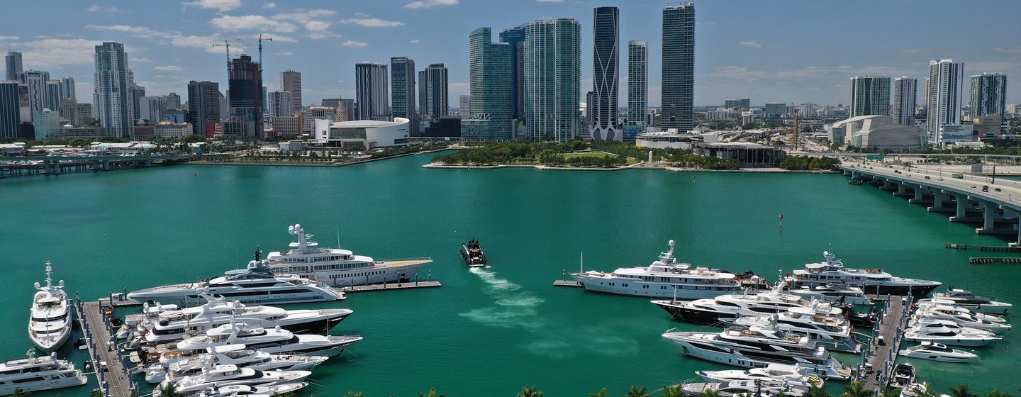 Overview of Yacht Haven Grande Miami at Island Gardens, multiple superyachts moored, looking at skyscrapers over the water.