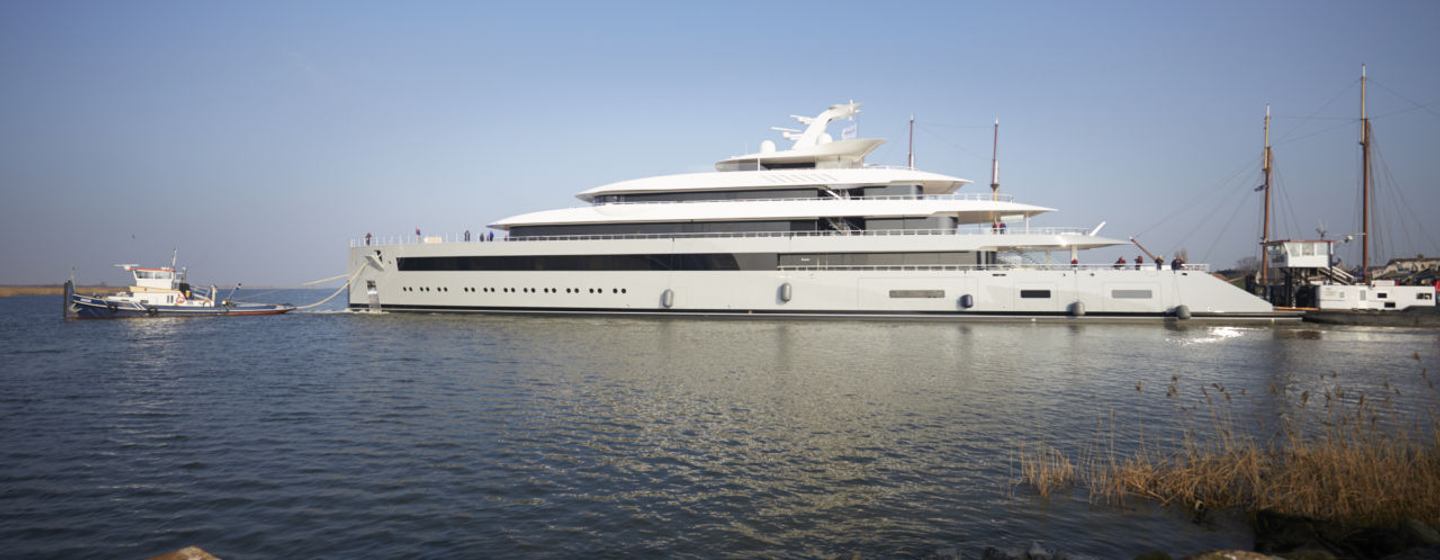 Feadship MOONRISE underway leaving the docks, surrounded by sea with rocks in foreground