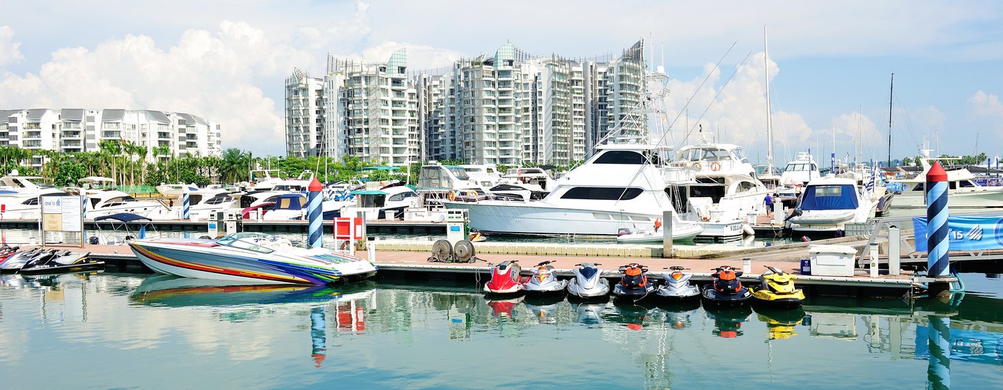 Water level view of Singapore Yacht Show, with multiple yachts moored and high rising buildings in background.