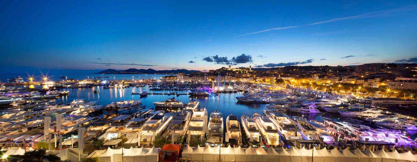 Overview of Cannes Yachting Festival at dusk, multiple motoryachts moored plus sailing boats in the bay