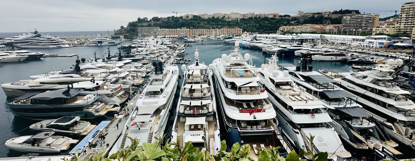 A wide angle photo of Monaco Yacht Show 2024's Port Hercule with many superyachts at berth