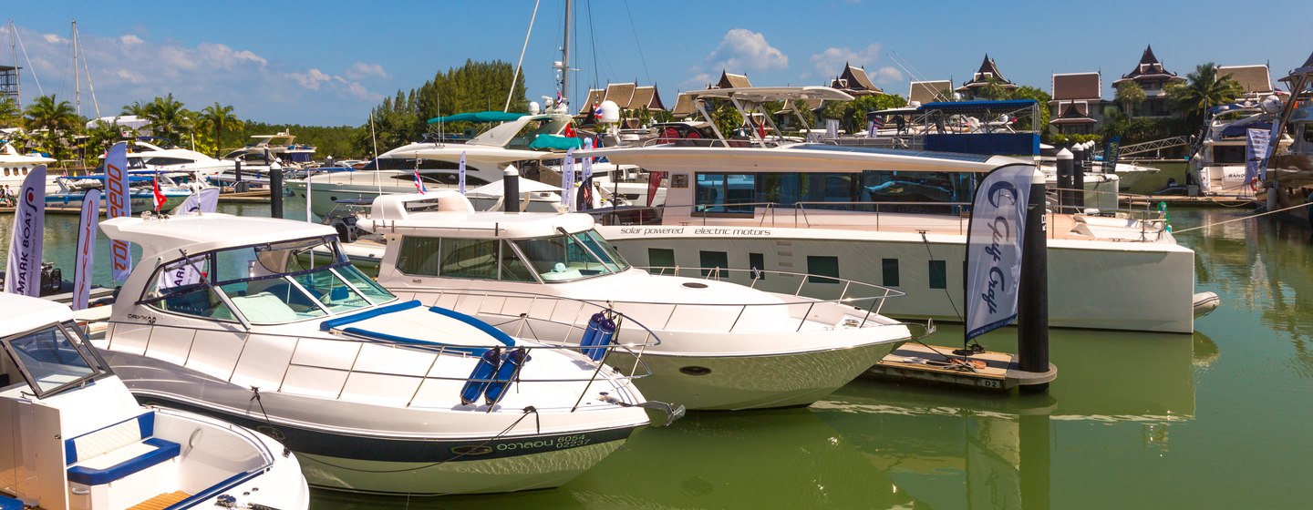 Motoryachts at anchor during Thailand Yacht Show, surrounded by green water and marina facilities in background