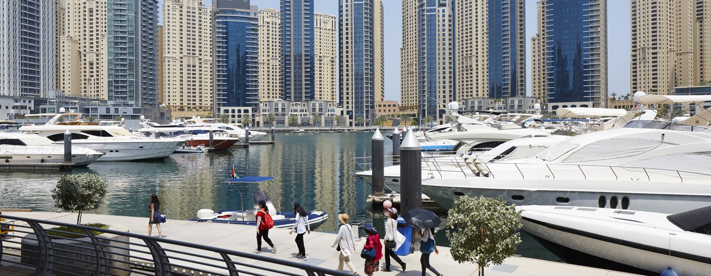 Guests walking along promenade at Dubai Harbour, multiple motor yachts moored with skyscrapers in background