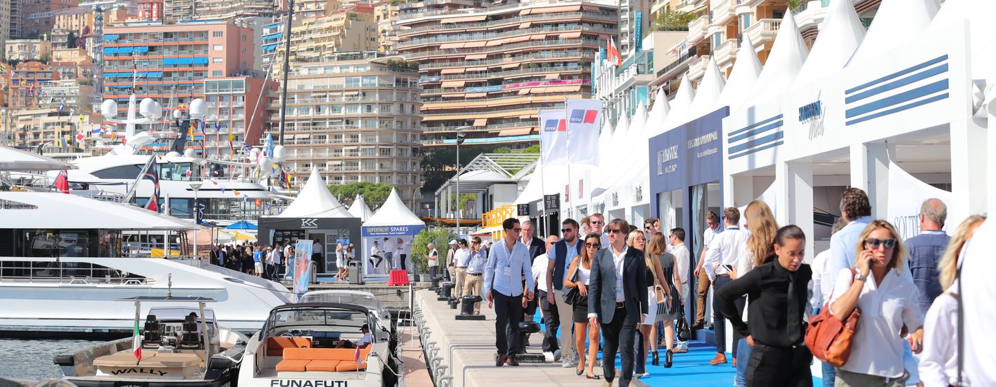 Crowd of people at Monaco Yacht Show, walking alongside a number of yachts moored in harbour