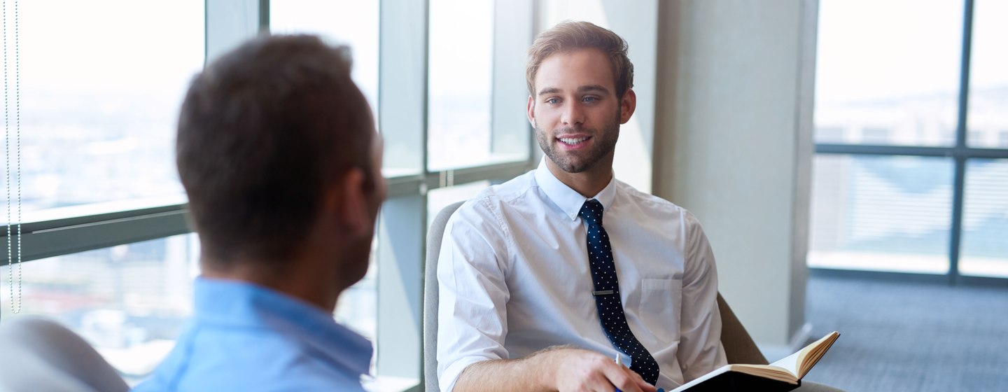 Young businessman sitting comfortably in an open modern office, smiling while having a positive conversation with a coworker