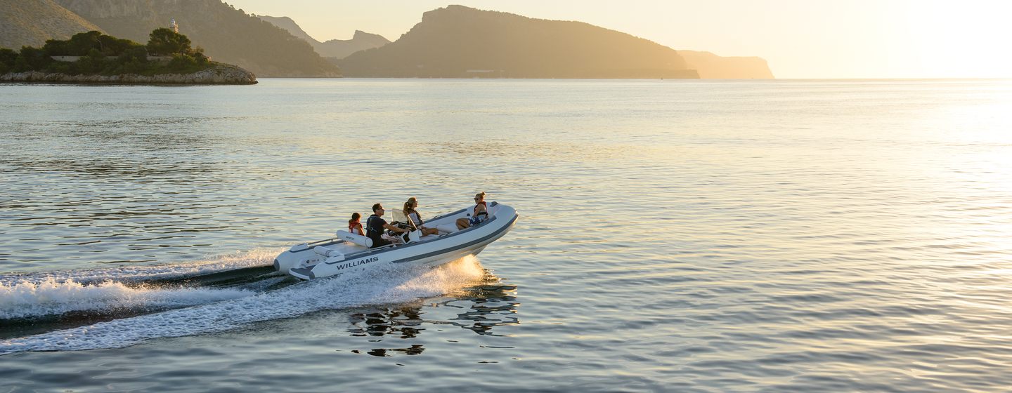 Williams SportJet 520 yacht tender running shot in calm waters at sunrsie, people onboard, starboard side profile, mountainous land in background