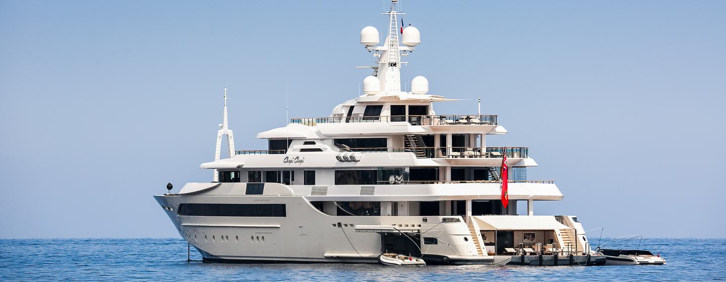 CRN 80m superyacht CHOPI CHOPI still in calm sea on bright day, distance shot at water level towards port aft deck showing side profile and open transom with shell doors open