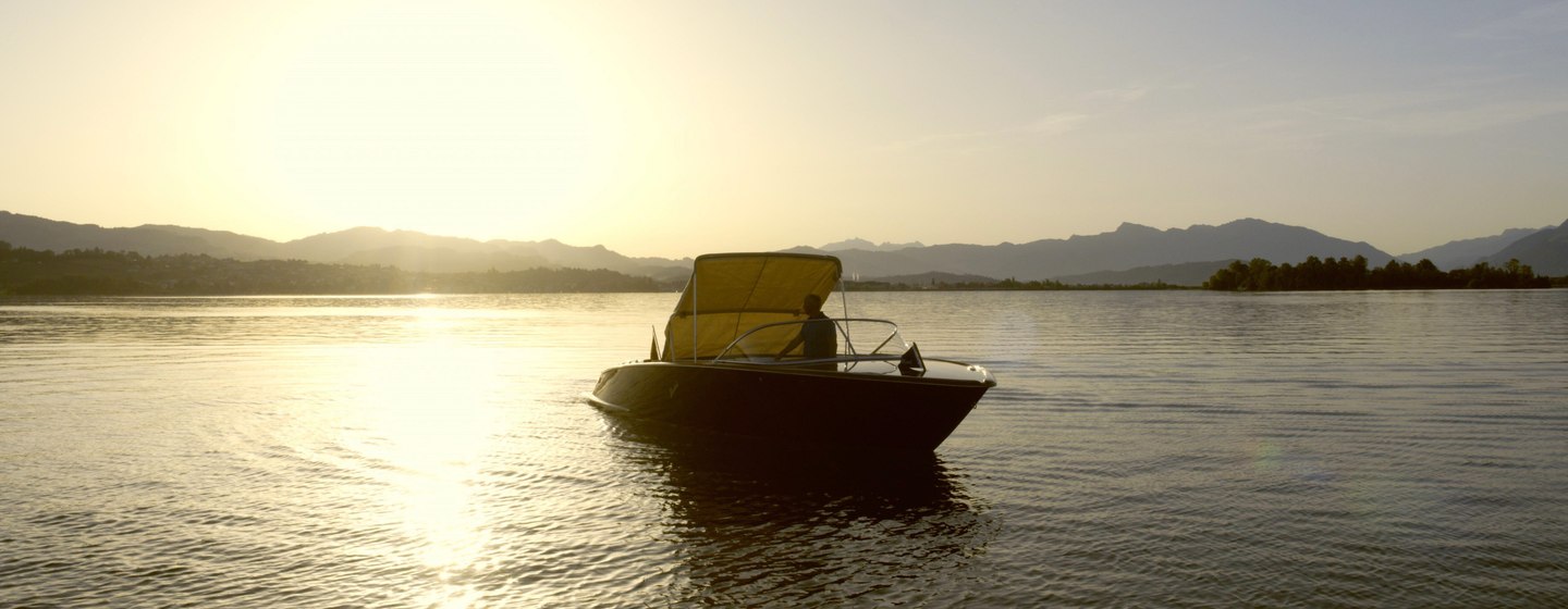 Tender boat on still water at sunset with hills in background