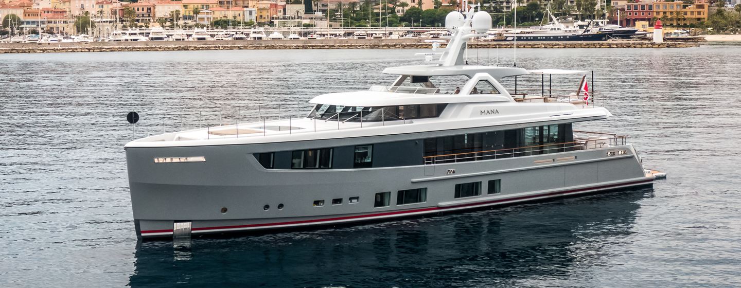 Mulder ThirtySix yacht MANA I port bow and side profile shown in aerial shot whilst on anchor in still waters, on grey day. Land in background