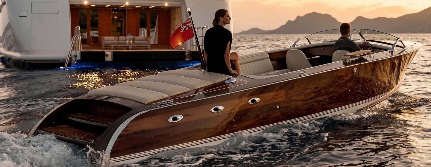 Classic tender boat with two guests on it in front of superyacht at dusk