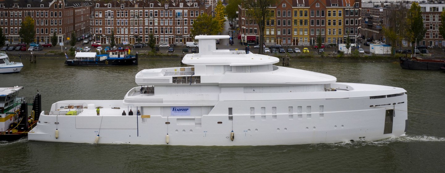 Feadship explorer yacht SHINKAI being towed, surrounded by cityscape in background and river