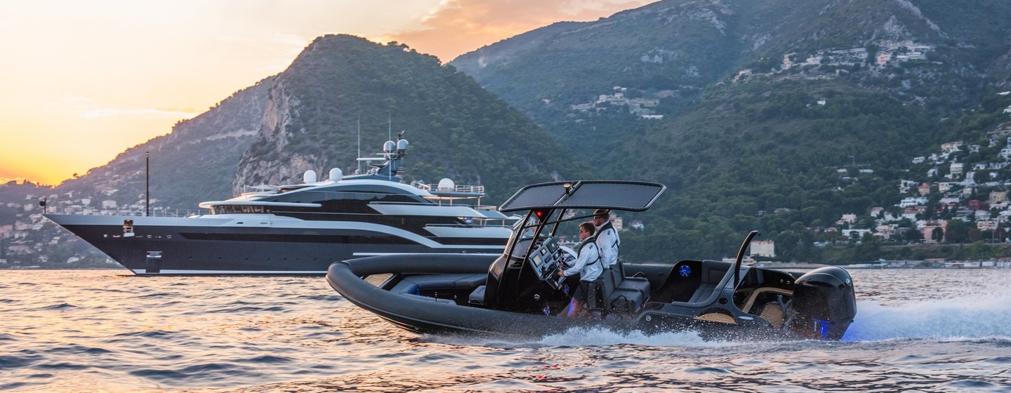 RIB tender boat with superyacht and mountainous coastline in the background