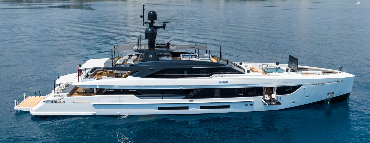 The starboard side of supryacht JIMMY at anchor in front of a mountainous backdrop