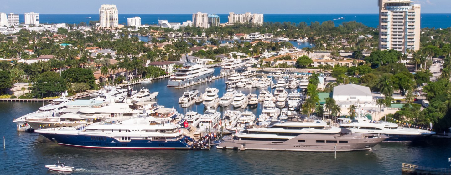 Elevated overview of FLIBS, causeway to starboard side, range of motor yachts moored to port side, sea on horizon