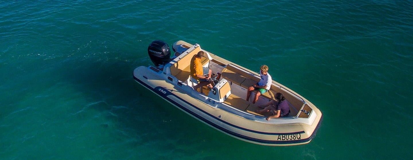 Three people on RIB tender viewed from above. RIB is still and on calm water.