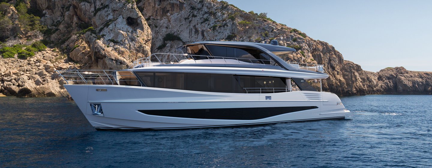 Motor yacht X90 at anchor, with rocky terrain in the background 
