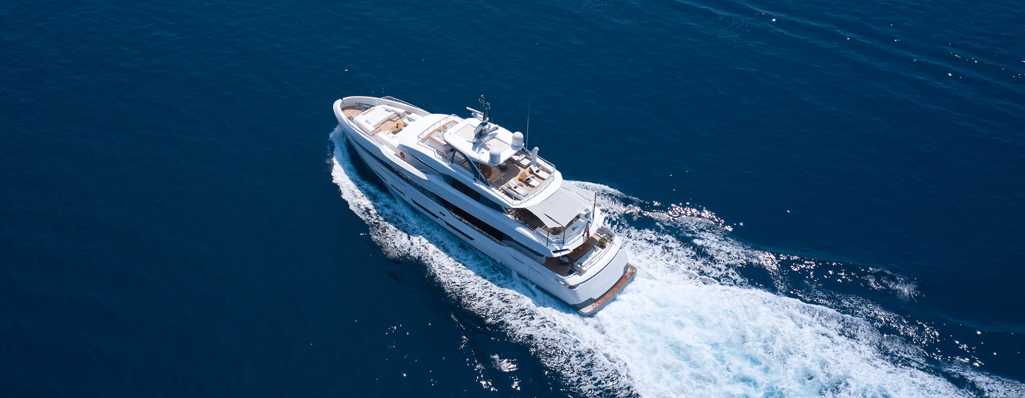 Aerial view of large superyacht underway, surrounded by sea heading towards the distance.