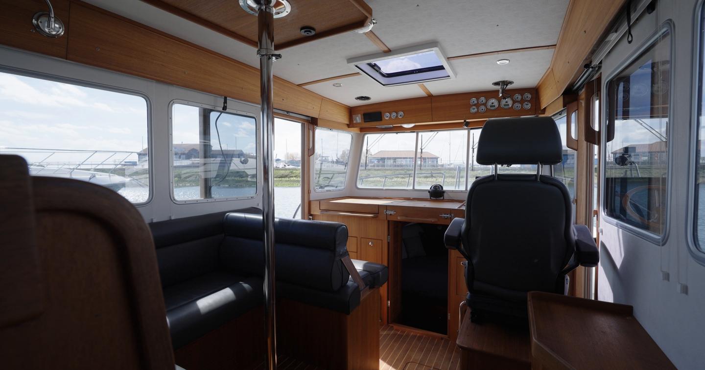 Botnia Targa 32 teak-lined wheelhouse with black saloon seating, central support pole, suspension helm seat and forward companionway.