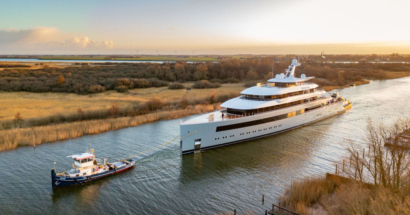 Aerial view of Feadship MOONRISE underway being escorted up a river, surrounded by vegetation