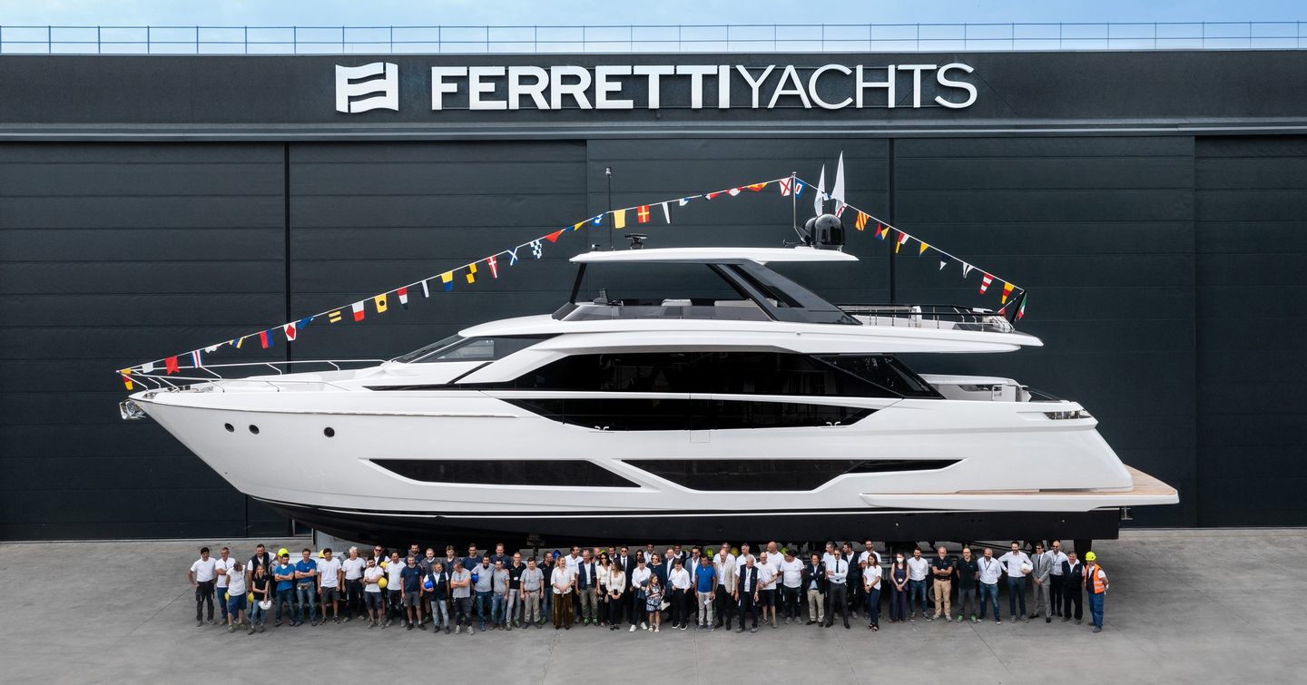 Ferretti Yachts 860 on tarmac in front of Ferretti Yachts logo, construction team stands in front posing for photo. 