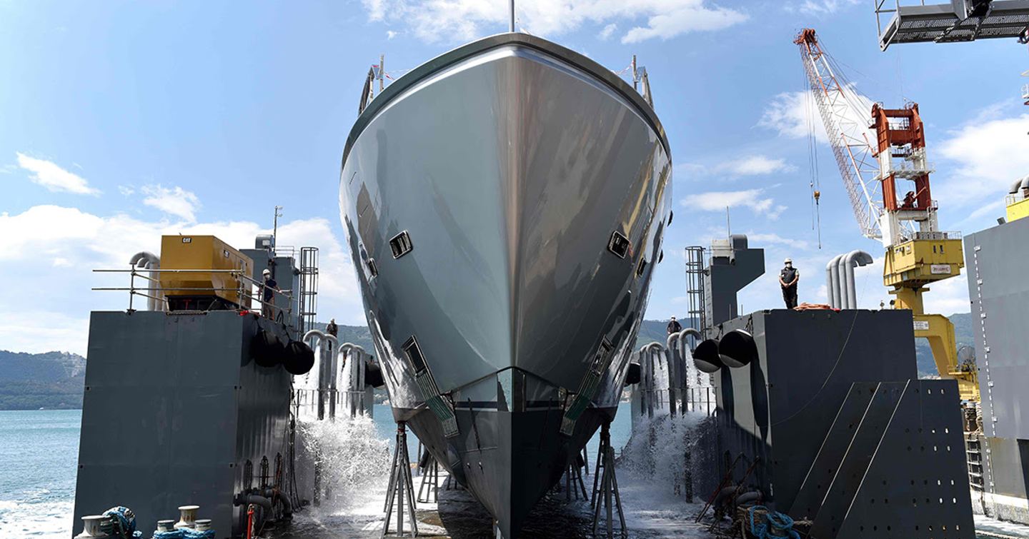 Frontal view of Sanlorenzo 44Alloy H1 hull in dock, surrounded by construction equipment, a crane and sea