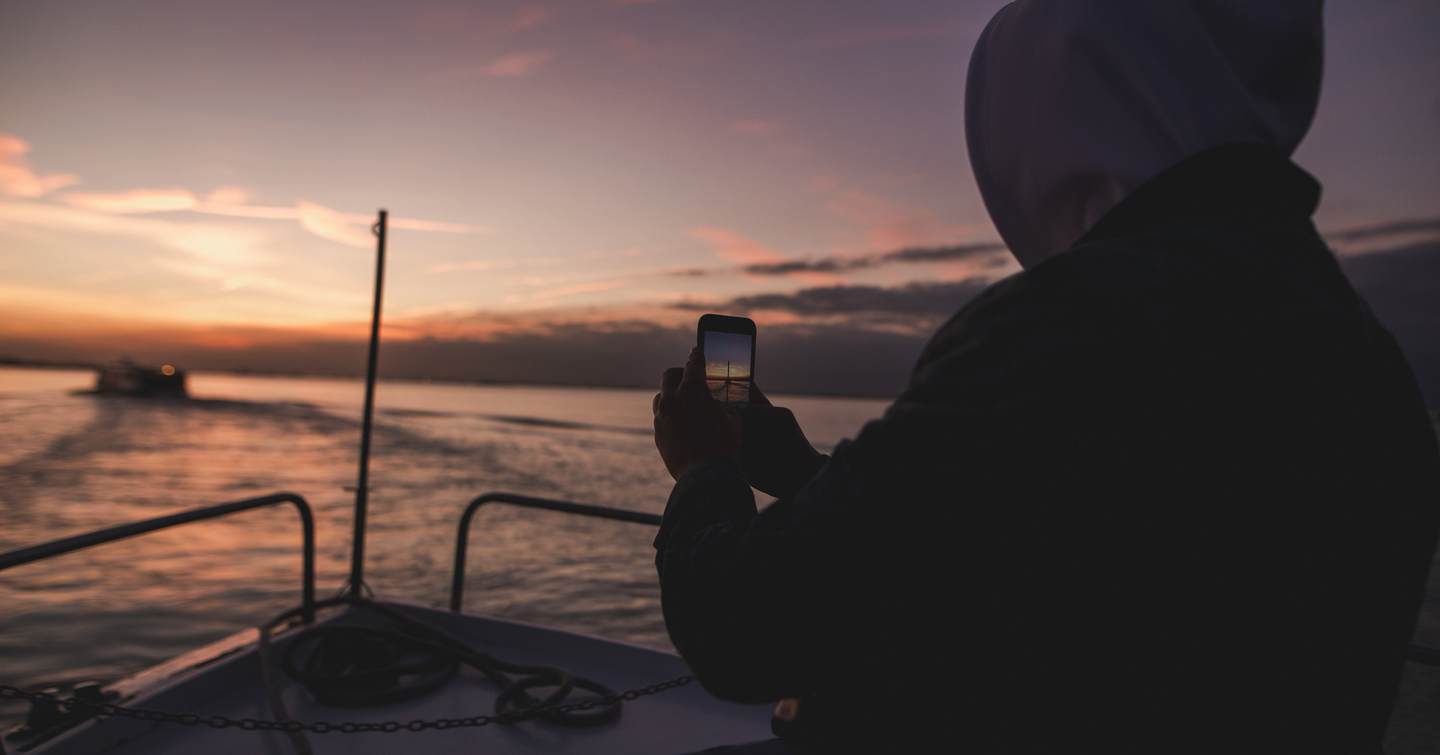 Person using a smartphone on a yacht deck at sunset