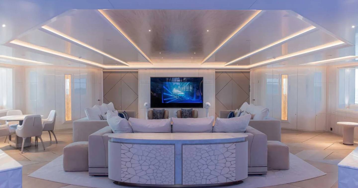 Overview of a lounge area onboard superyacht H3, with seating all facing in towards each other in the centre with a small table and chairs to port.