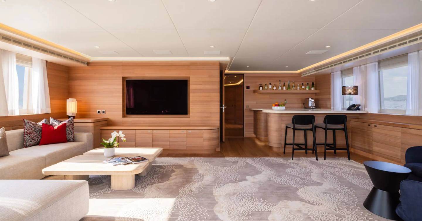 Expedition yacht Bijin saloon with L-shaped beige seating and wooden bar area 