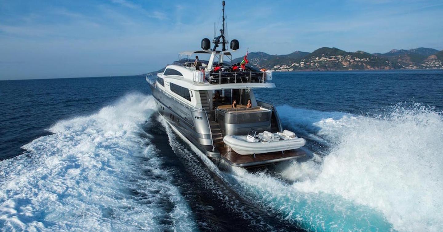 Aft view of superyacht O NOSO UNO underway, surrounded by sea foam and land in the far distance.