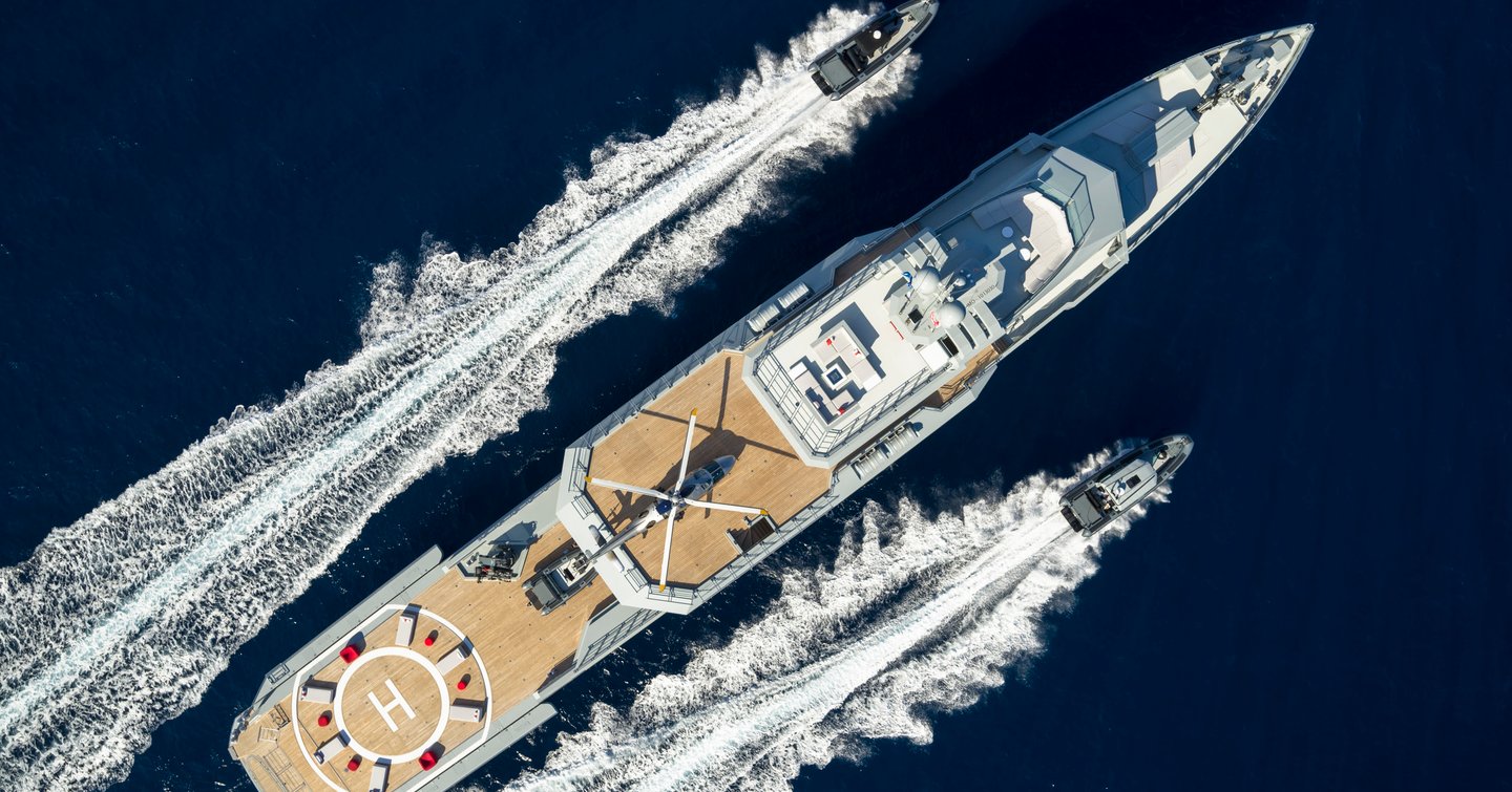 Bird's eye view of superyacht BOLD. Tenders speeding along either side, surrounded by sea.