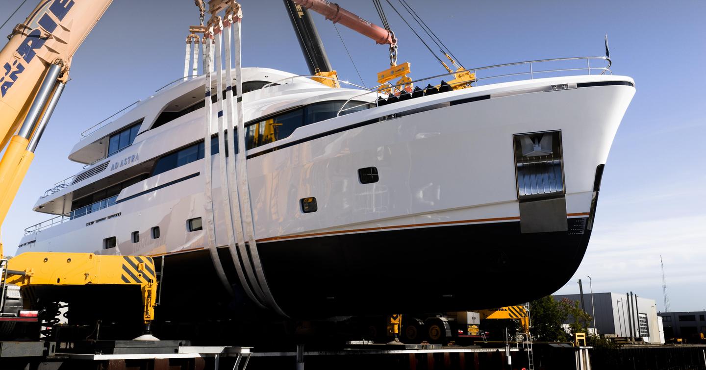 Motor yacht Ad Astra being lowered into the water by cranes during her launch, with hull straps supporting the vessel.