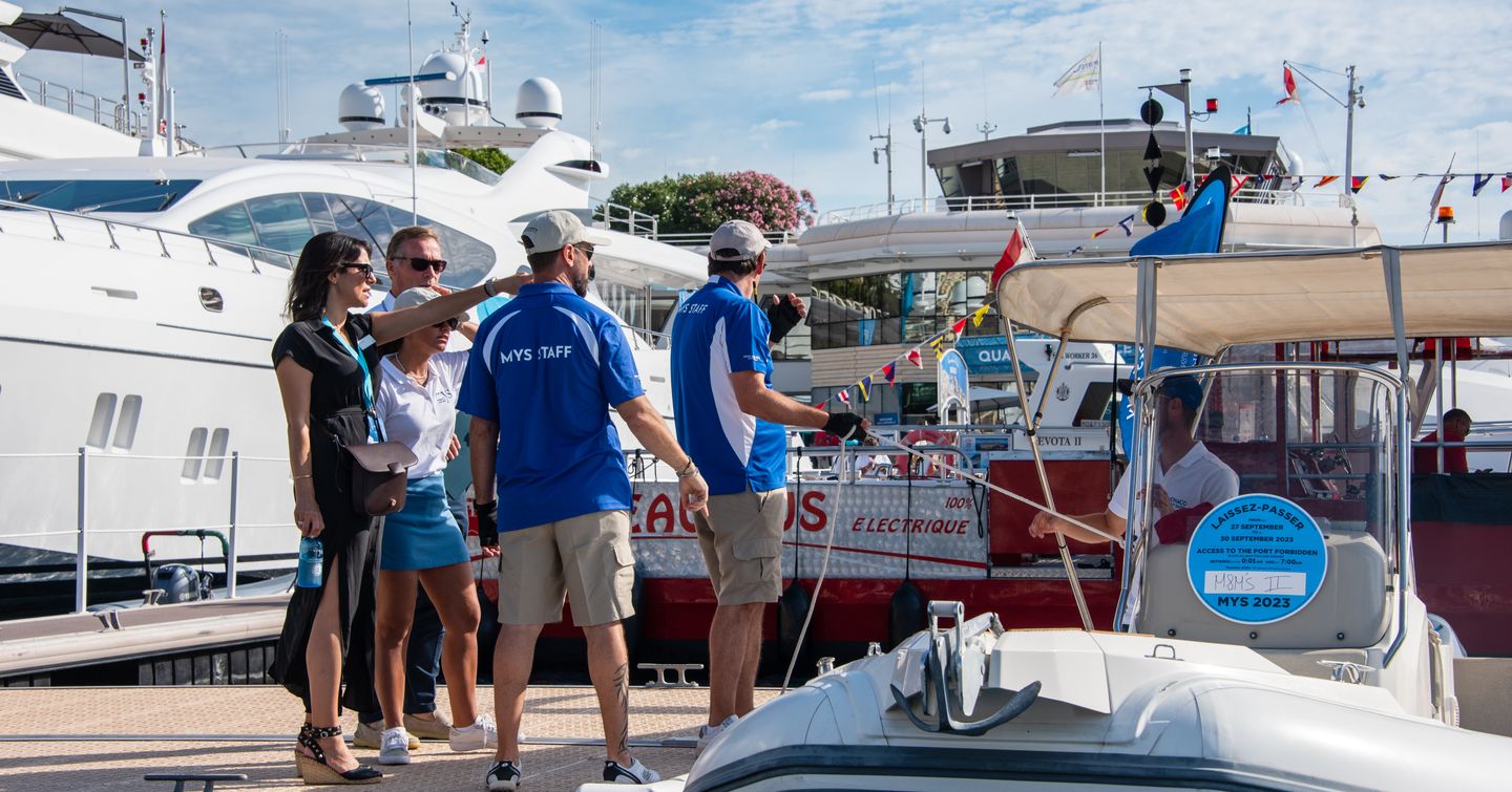 Visitors at the Monaco Yacht Show speaking to crew members next to some superyachts