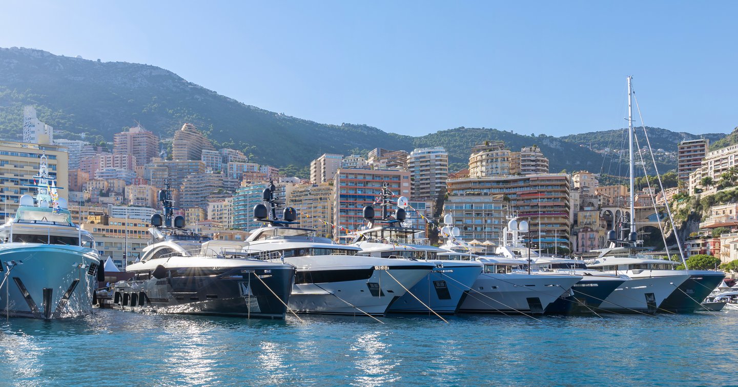 Line of motor yachts berthed at Monaco Yacht Show, Monte Carlo in background.