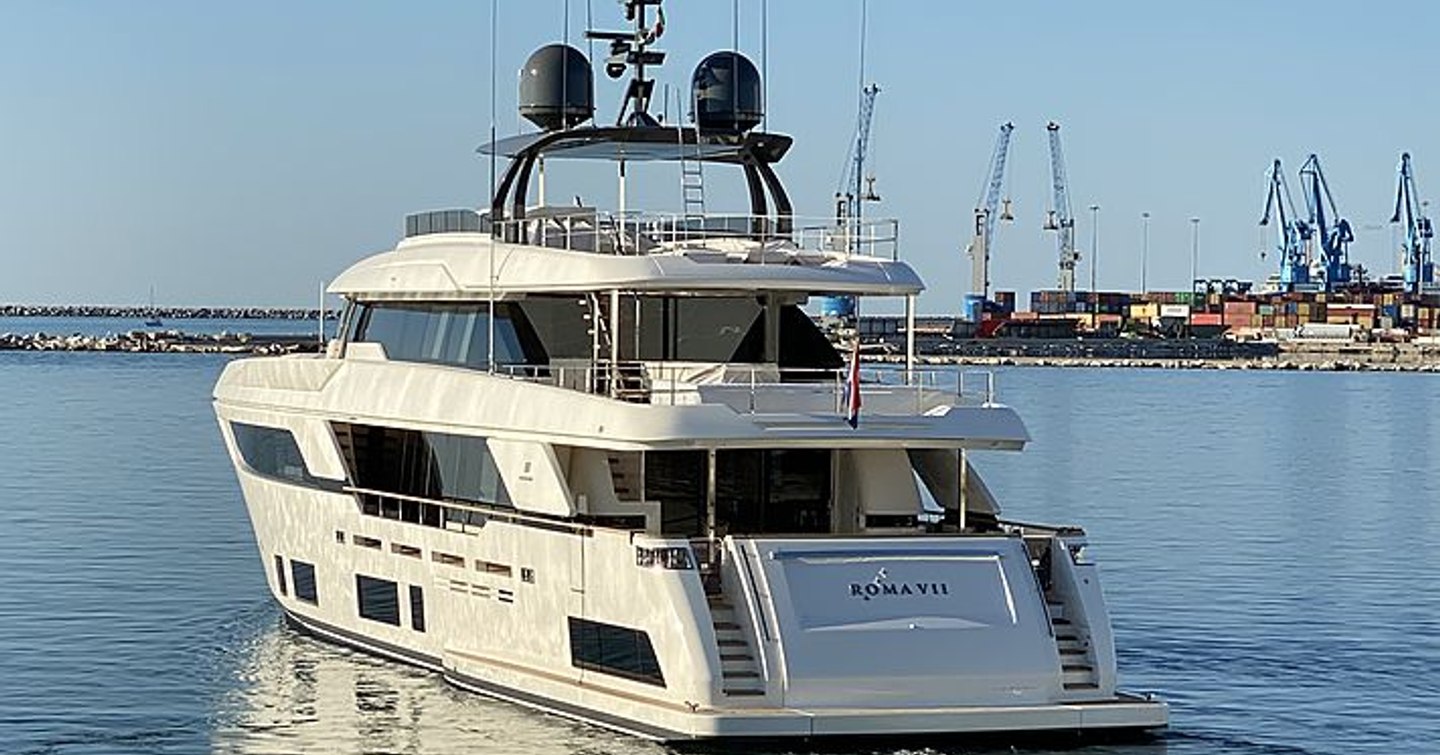 Aft view of Custom Line ROMA VII underway, surrounded by sea and distant construction yard in background