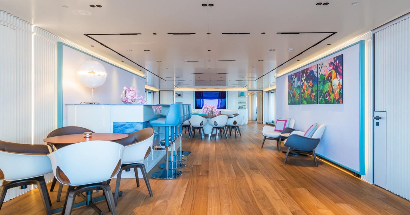 Motor yacht Rio's dining area with two round tables, a bar area and teak flooring