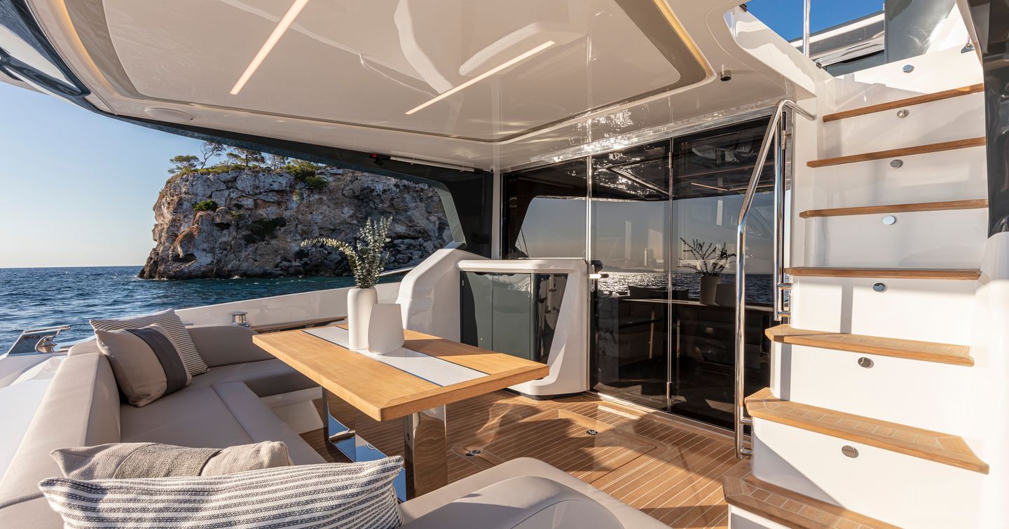 Overview of aft deck onboard Pearl 62, C shaped seating and dining table facing stairs to flybridge