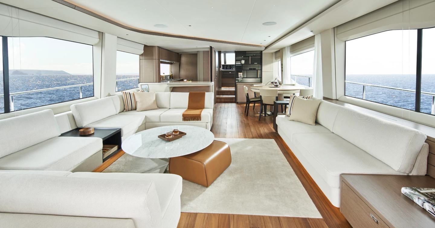 Main salon onboard Princess Y85, sofas to port and starboard with coffee table central and dining area aft.