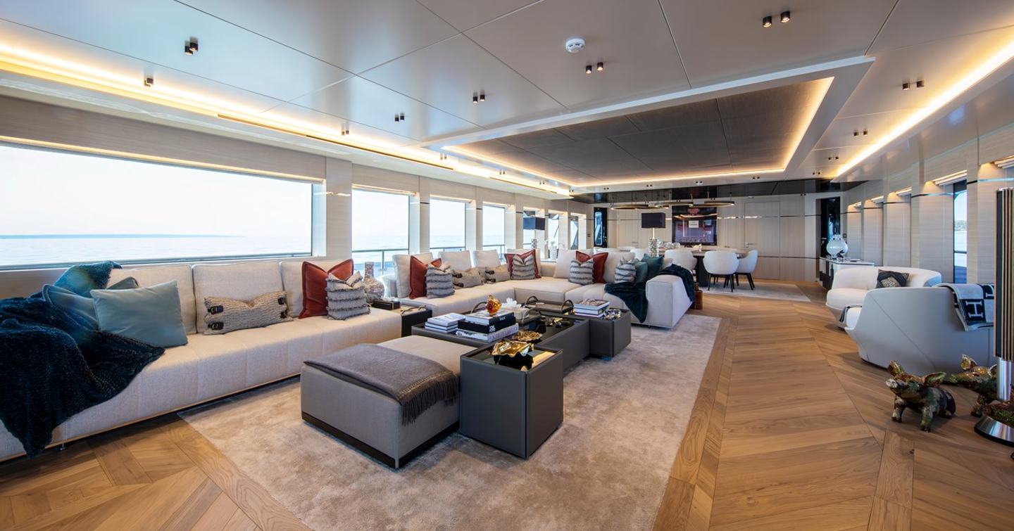 Superyacht Oscar's main saloon with L-shaped grey seating and dining area 