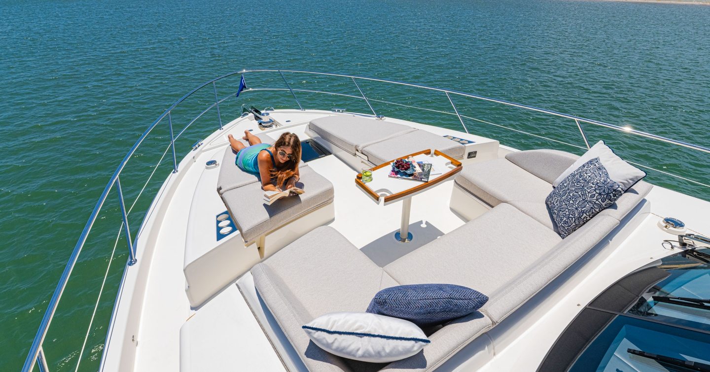 Woman sunbathing on Riviera 5600 Sport Yacht Platinum Edition motor yacht foredeck next to U-shaped grey seating