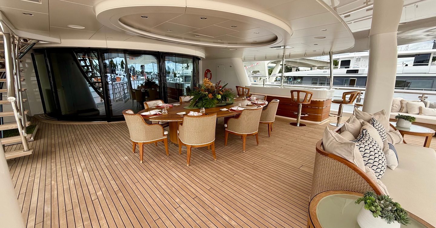 Outdoor dining area on the owner's deck of the Amels 242 Casino Royale with round table and bar behind.