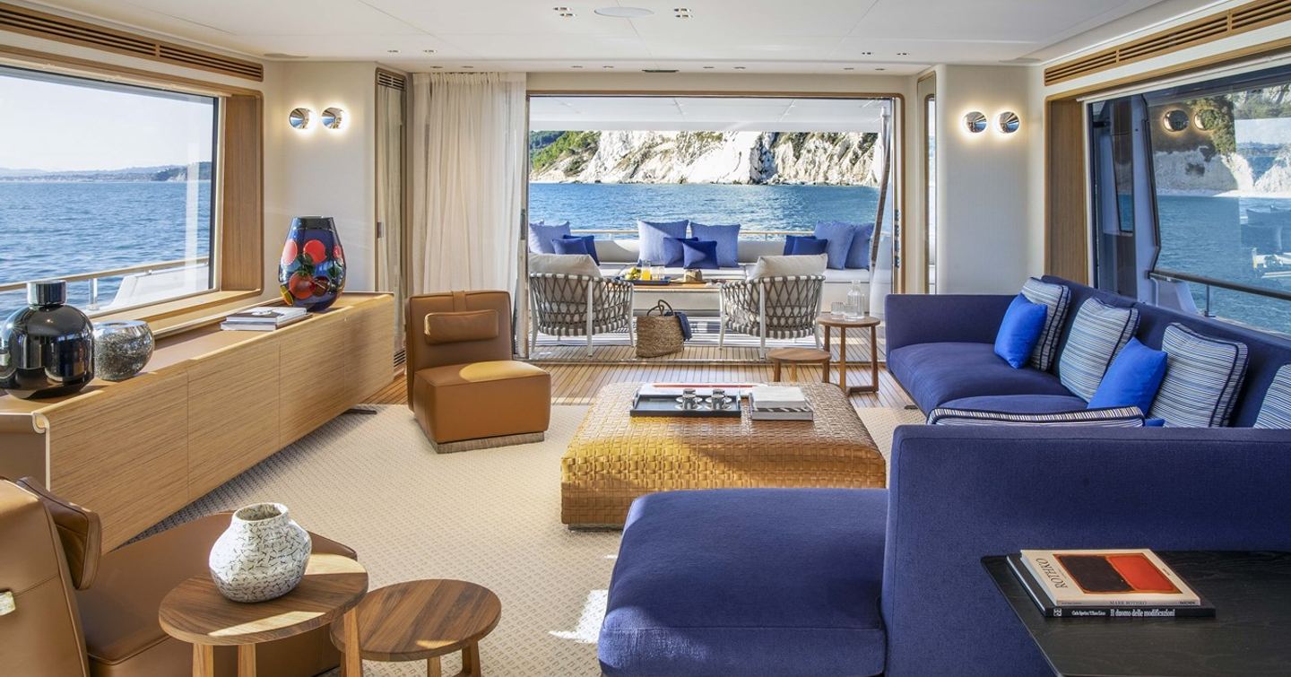 Motor yacht Numero Dix main saloon with L-shaped blue sofa and woven coffee table