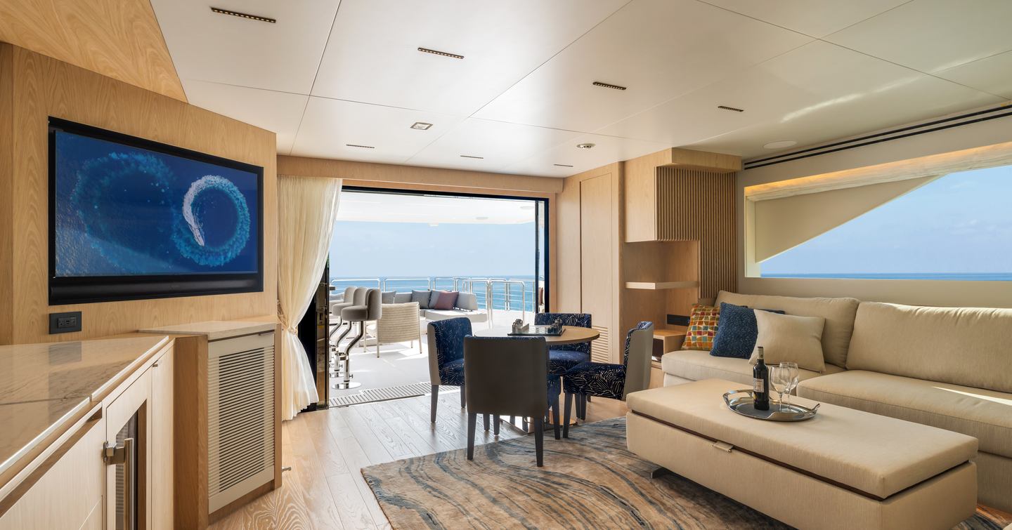 Seventh Horizon FD110 motor yacht skylounge with mounted TV, white sofa and circular wooden table 