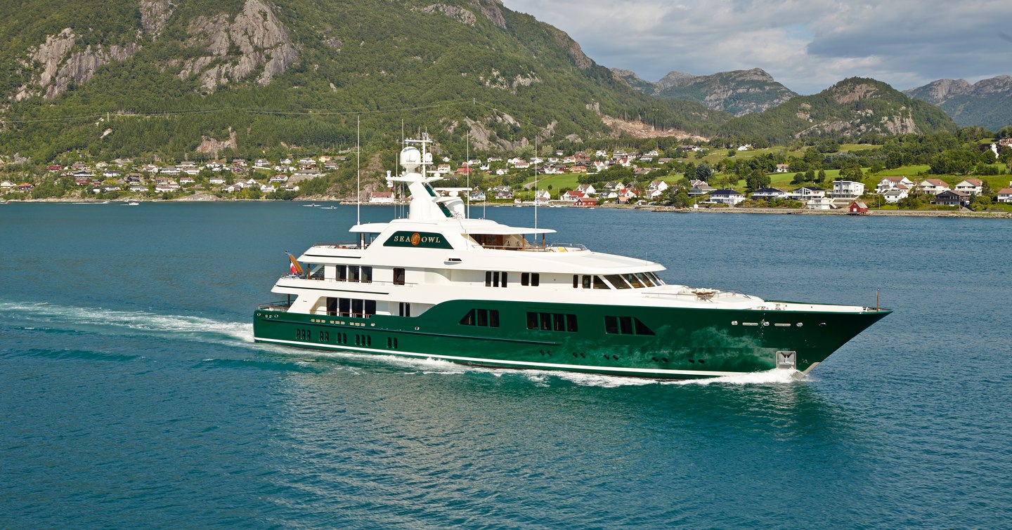 Superyacht Sea Owl underway, surrounded by sea and mountains in background.